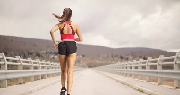 一名身穿运动服的女子从桥上跑过去的后视镜照片 — 图库照片