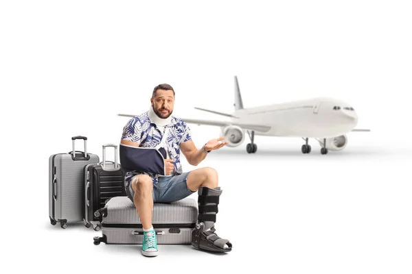 負傷した腕と脚をスーツケースに座って白い背景に隔離された飛行機を待っている男性観光客を失望させました — ストック写真