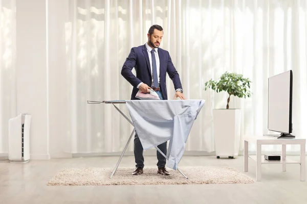 ビジネスマンはリビングでテレビの前で家でシャツをアイロンをかける — ストック写真