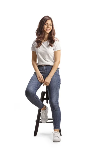 穿着牛仔裤和白色T恤衫的年轻貌美的女人坐在高椅上 孤零零地坐在白色的背衬上 — 图库照片