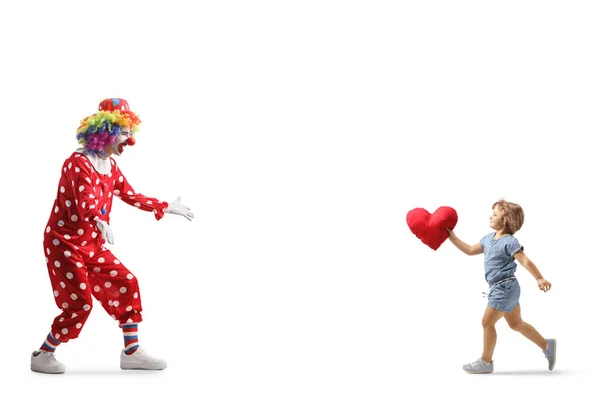 一个小女孩抱着心脏跑去拥抱一个被白色背景隔离的小丑的全景镜头 — 图库照片