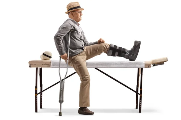 老年男性患者坐在理疗床上 腿上的支架与白色背景隔离 — 图库照片