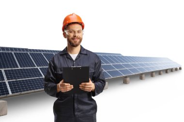 Beyaz arka planda izole edilmiş fotovoltaik bir alanda gözlüklü ve kasklı bir teknisyen elinde bir pano tutuyor.