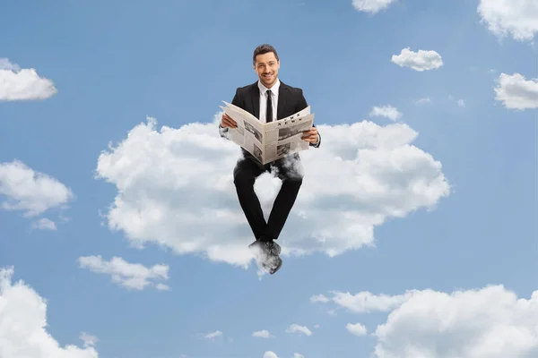雲の上に座って空に新聞を読むスーツのプロの若者 — ストック写真