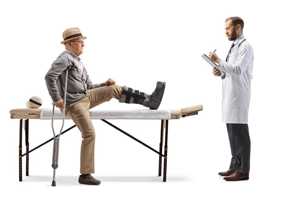 医生开处方 一位老年男性病人坐在理疗床上 腿上的支撑物与白色背景隔离 — 图库照片