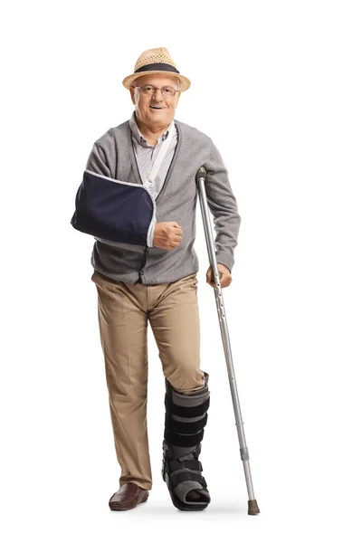 白い背景に隔離された松葉杖にもたれかかる骨折した腕と歩行ブレースを持つ高齢者 — ストック写真