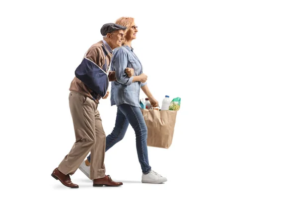 一名妇女用受伤的胳膊帮助一名老年男子 并提着用白色背景隔开的购物袋的全景照片 — 图库照片