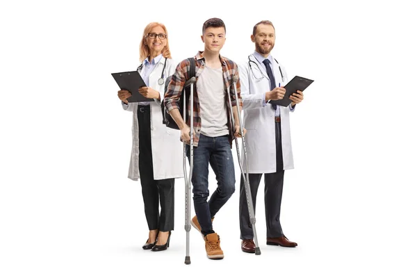 白い背景に孤立した松葉杖を持つ男性学生の後ろの医師のチーム — ストック写真