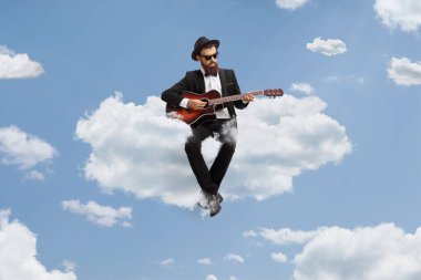 Adam akustik gitar çalıyor ve gökyüzünde bir bulutun üzerinde oturuyor.