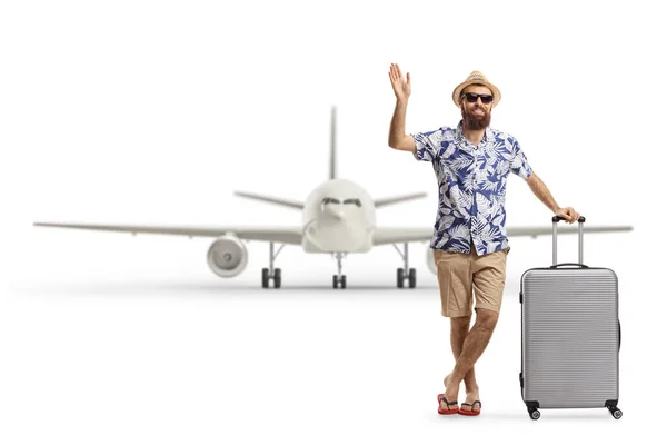 スーツケースを背負った髭の男の観光客の完全な長さの肖像画と白い背景に隔離された飛行機の前で手を振る — ストック写真