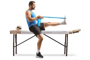 Adam terapi yatağında beyaz arka planda izole edilmiş bir direniş bandıyla egzersiz yapıyor.