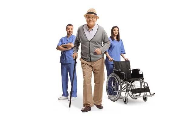 白い背景に隔離された医療従事者のチームの前で杖を持つ高齢者 — ストック写真