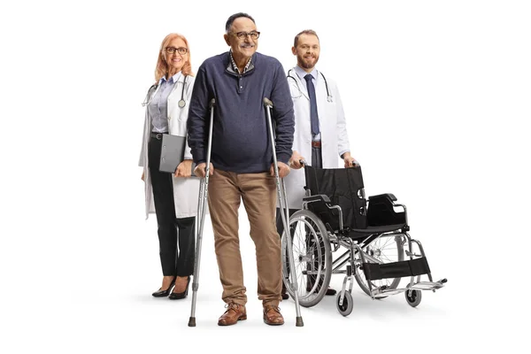 白い背景に松葉杖を持つ患者の後ろに車椅子を持つ医師 — ストック写真
