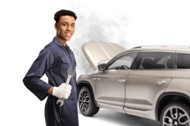 Beyaz arka planda izole edilmiş bir şekilde İngiliz anahtarı tutan ve gülümseyen bir SUV 'un önünde duran Afrikalı Amerikalı araba tamircisi.