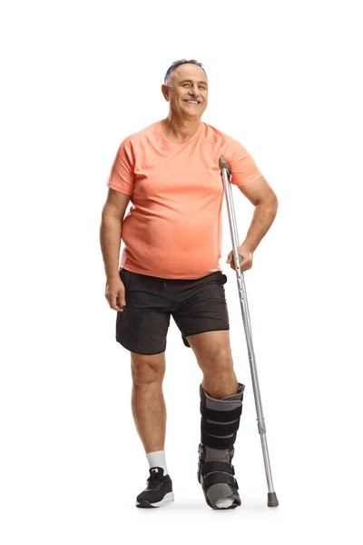 白い背景に隔離された松葉杖にもたれて歩くブレースを持つスポーツウェアの熟女 — ストック写真