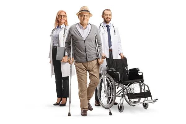Médicos Com Uma Cadeira Rodas Atrás Paciente Sênior Com Muletas — Fotografia de Stock