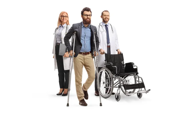 白地に松葉杖を持った髭の男の後ろに車椅子を背負った医者がいる — ストック写真