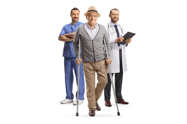 白い背景に隔離された背中に松葉杖と医療従事者を持つ高齢者の完全な長さの肖像画 — ストック写真