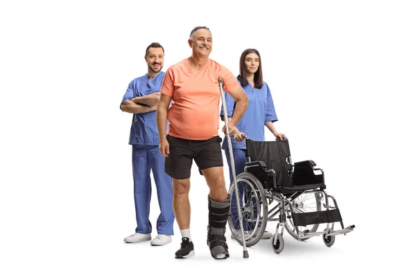 白い背景に隔離された医療従事者と整形外科のブーツと松葉杖を持つ成熟した男性患者 — ストック写真
