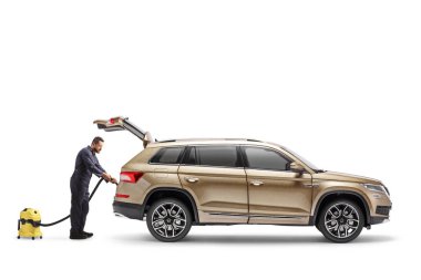 Beyaz arka planda izole edilmiş elektrikli süpürgeyle SUV temizleyen bir işçi.