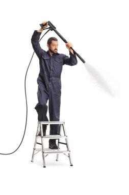 Üniformalı bir adam basınçlı çamaşır makinesi kullanıyor ve beyaz arka planda izole edilmiş bir merdivenin üzerinde duruyor.