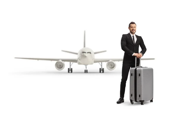 白い背景に隔離された飛行機の前でスーツケースを身に着けてポーズをとるプロの男の完全な長さの肖像画 — ストック写真
