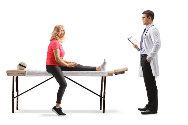 負傷した足を持つ女性は治療台の上に座って 白い背景に隔離された男性医師と話をします — ストック写真