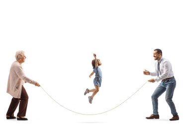 Baba ve büyükanne beyaz arka planda izole edilmiş küçük bir kızla ip atlama oyunu oynuyorlar.