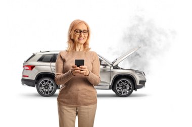 Akıllı telefondan yazı yazan ve beyaz arka planda dumanlı kaputu açık bir SUV 'nin önünde duran bir kadın.