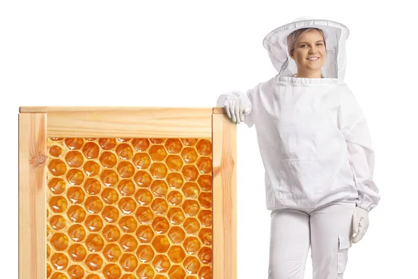 白い背景に隔離された大きなハニカムフレームにもたれている制服を着た女性養蜂家 — ストック写真