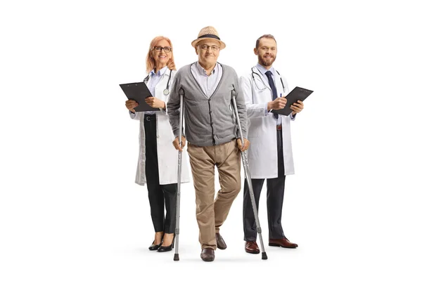 白い背景に隔離された背中に松葉杖と医師を持つ高齢男性患者の完全な長さの肖像画 — ストック写真