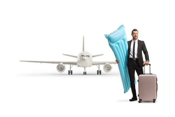 白い背景に隔離された飛行機の前にフローティングマットレスとスーツケースを持つビジネスマン — ストック写真