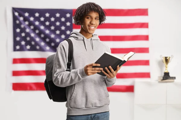 Male african american student standing and reading a book in front of a USA flag