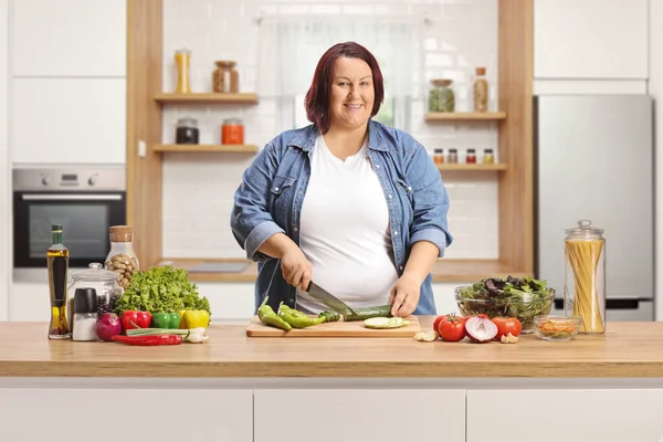 台所のカウンターで野菜を切る太りすぎの女性と笑顔 — ストック写真