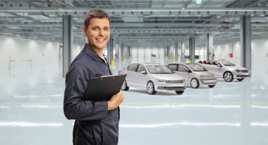 Araba tamircisi elinde bir dosya ve park halindeki araçların önünde bir faktör tutuyor.