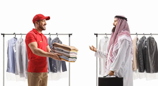 Man delivering pile of ironed clothes to an arab man in ethnic clothes isolated on a white backgroun
