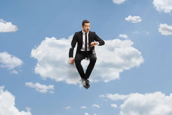 雲の上に座って時計をチェックするビジネスマンの完全な長さの肖像画 — ストック写真