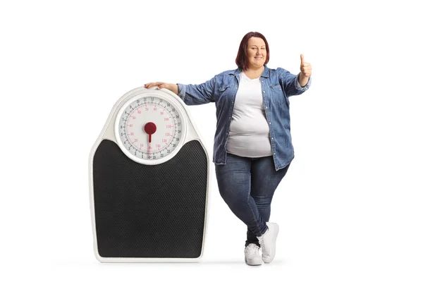 医学的スケールの隣に立つ太りすぎの女性とジェスチャー親指アップ白の背景に隔離 — ストック写真