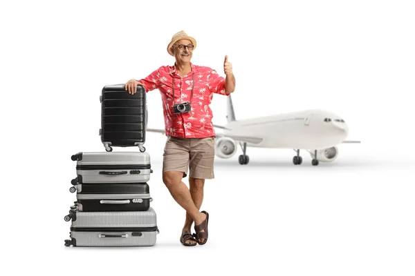 一个成熟男人靠在一堆行李箱上 在白色背景隔离的飞机前竖起大拇指的全长肖像 — 图库照片