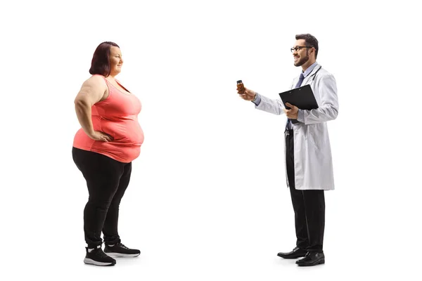 医師の完全な長さのプロフィールショットは 白い背景に隔離された太りすぎの若い女性に丸薬のボトルを与えます — ストック写真