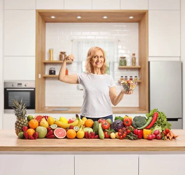 台所のカウンターで果物や野菜の後ろにサラダのボウルを保持幸せな強い女性 — ストック写真