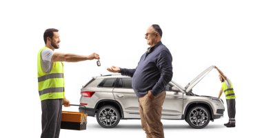 Tamirci bir SUV 'yi kontrol ediyor ve beyaz arka planda izole edilmiş olgun bir adama araba anahtarları veriyor.