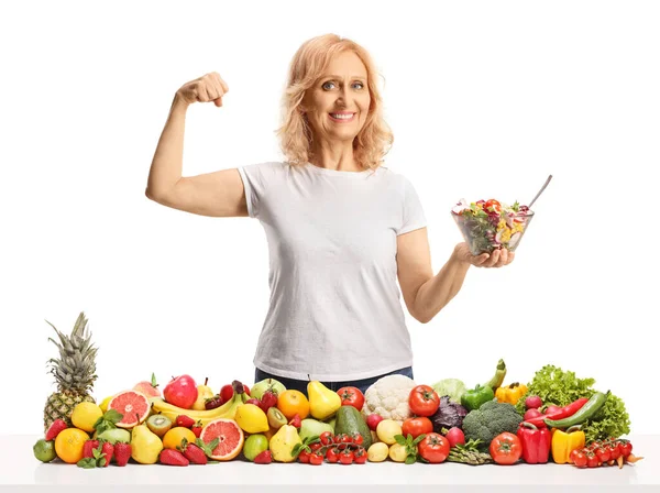 一个成熟的女人在水果和蔬菜后面拿着一碗沙拉 在白色背景下面带微笑 — 图库照片
