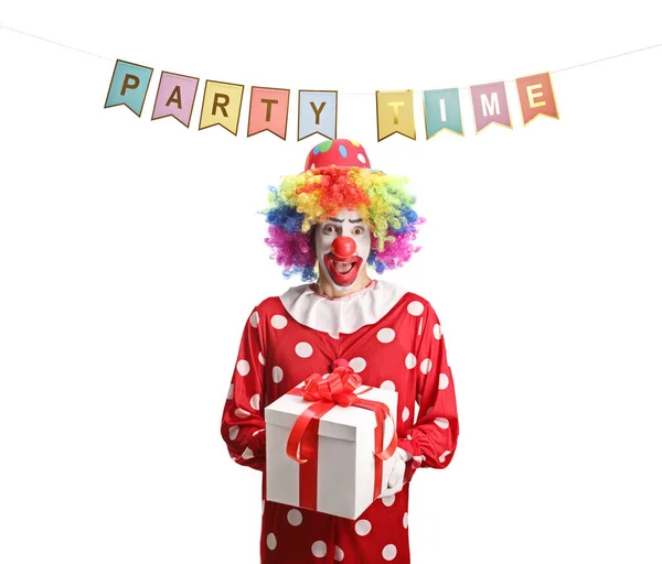 在党的旗帜下穿着红色服装的小丑拿着一个白色背景的礼盒 — 图库照片