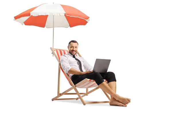 ビジネスマンは 傘の下のデッキチェアに座って 白い背景に隔離されたラップトップコンピュータを使用して — ストック写真