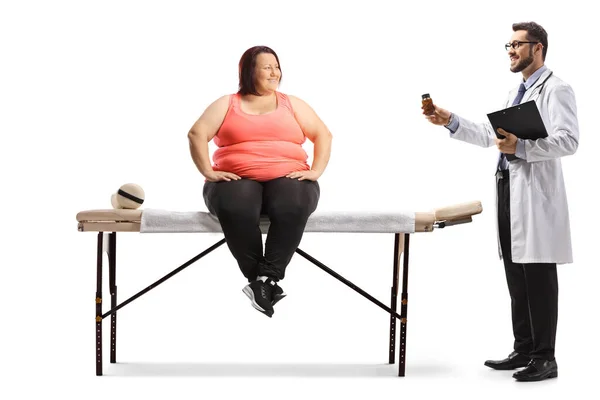 白い背景に隔離された薬のボトルを示す物理療法のテーブルと医者に座っている太りすぎの女性 — ストック写真