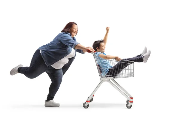 白い背景に隔離されたショッピングカート内で男の子を押す太りすぎの女性の完全な長さのプロフィールショット — ストック写真