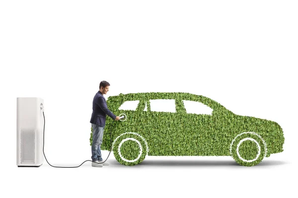 白い背景に隔離された草で作られた緑の車のためのEv充電器を使用して男 — ストック写真