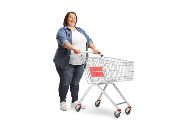 白い背景に隔離された空のショッピングカートで立っている太りすぎの女性の完全な長さのショット — ストック写真