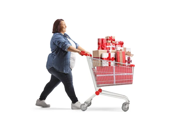 白い背景に隔離されたショッピングカートでプレゼントと歩く太りすぎの女性の完全な長さのプロフィールショット — ストック写真